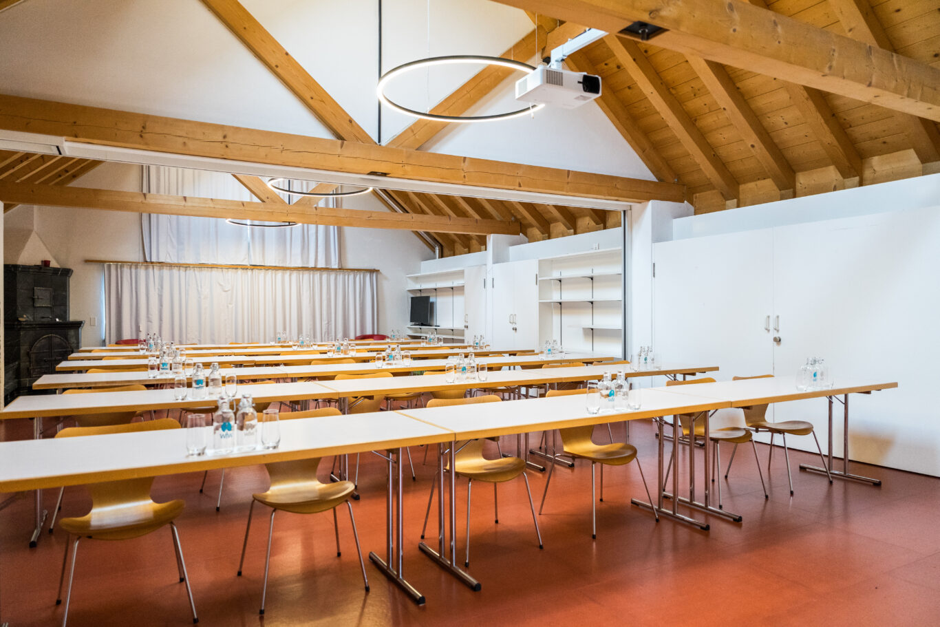 Moderner Seminarraum mit Holzbalkendecke, weißen Tischen und Stühlen.