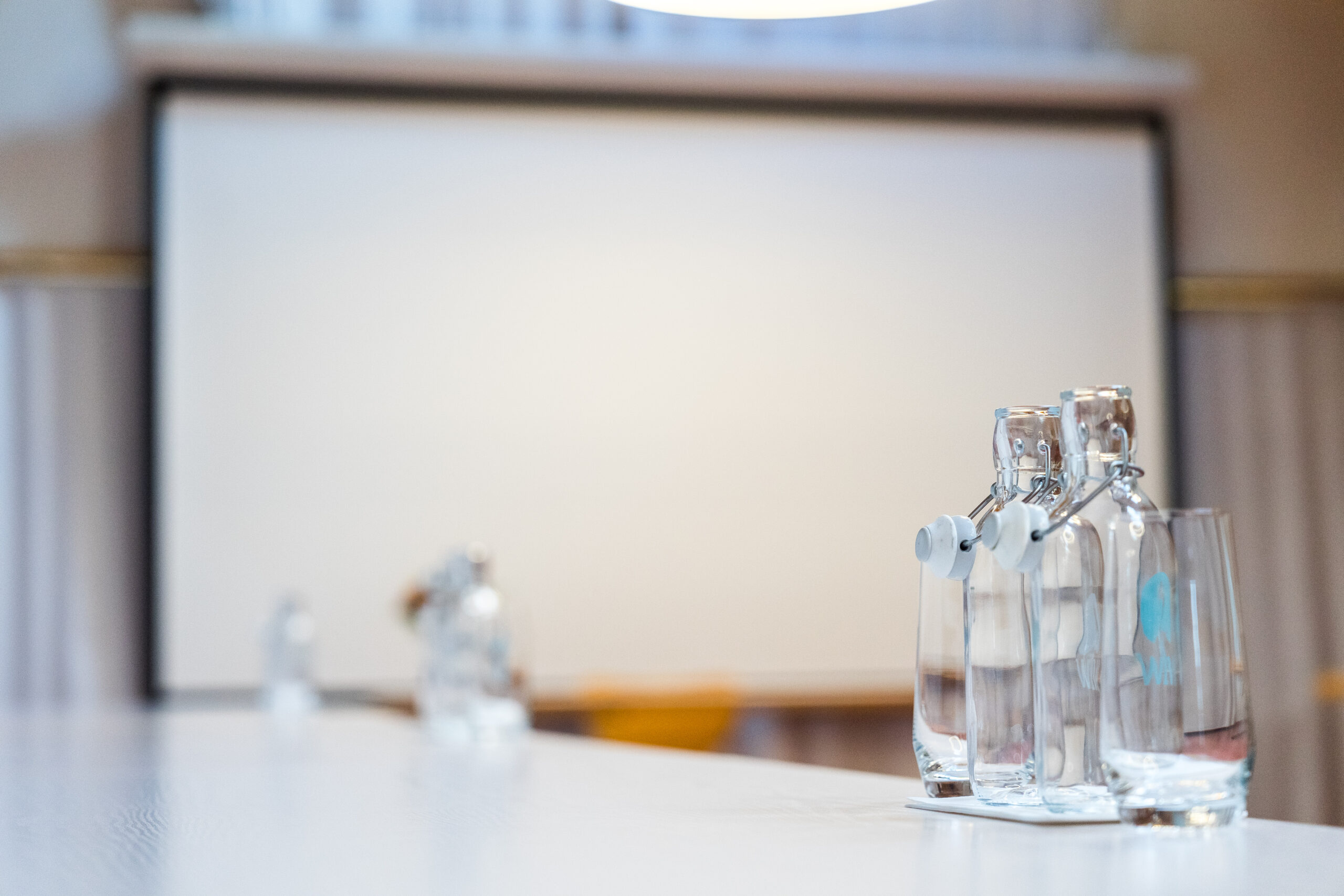 Glasflaschen und Gläser auf Tisch vor weißer Leinwand.