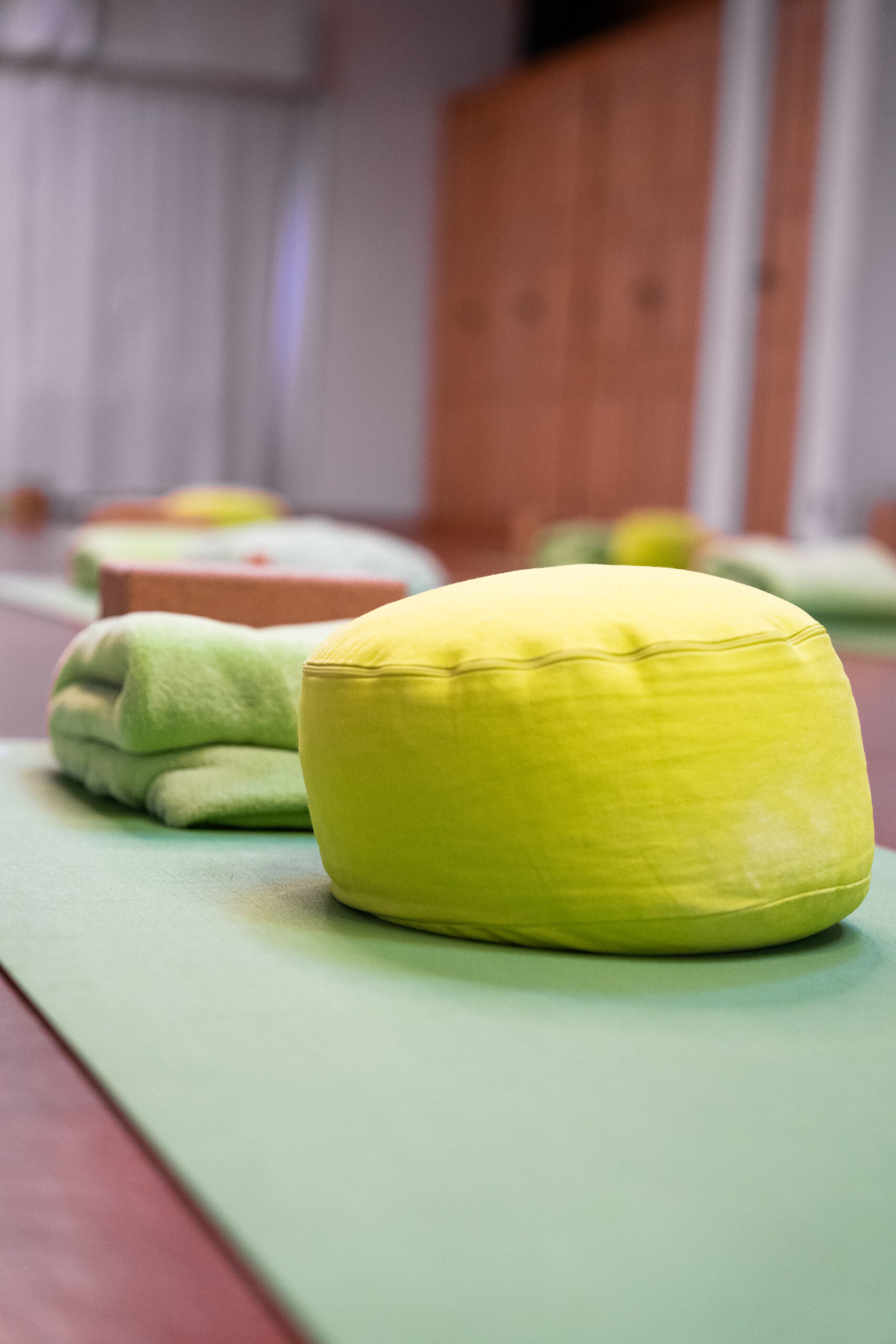 Meditationskissen, Decke und Yogablock auf einer grünen Matte.