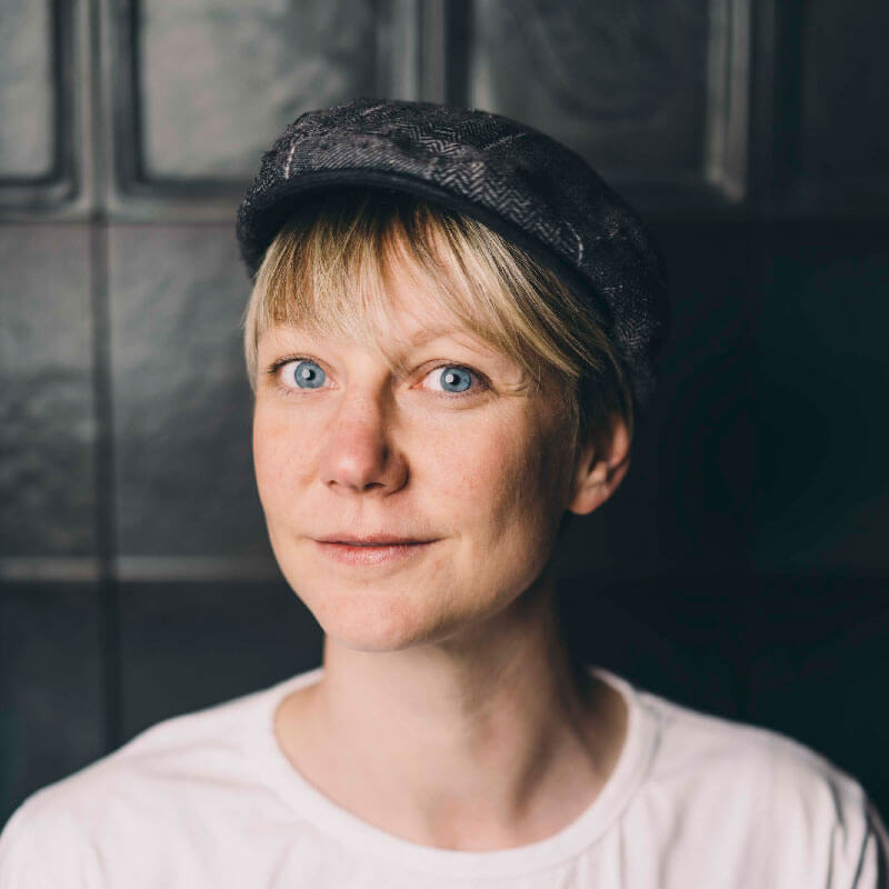 Portrait einer Frau mit blonder Kurzhaarfrisur und grauer Schiebermütze.