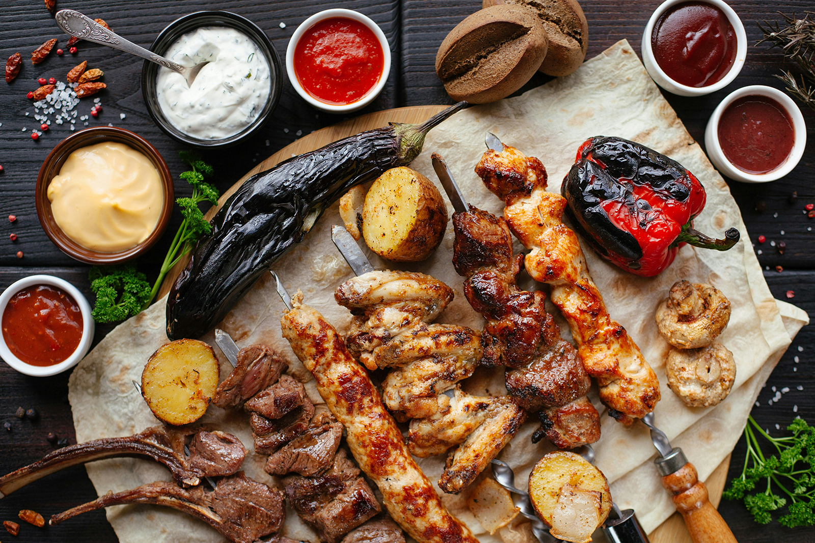 Verschiedene Grillspieße, Fleisch und Gemüse mit Saucen auf Fladenbrot.