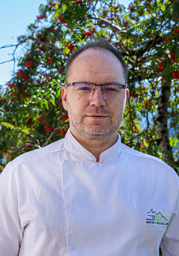 Koch in weißer Arbeitskleidung vor einem Baum mit Beeren.