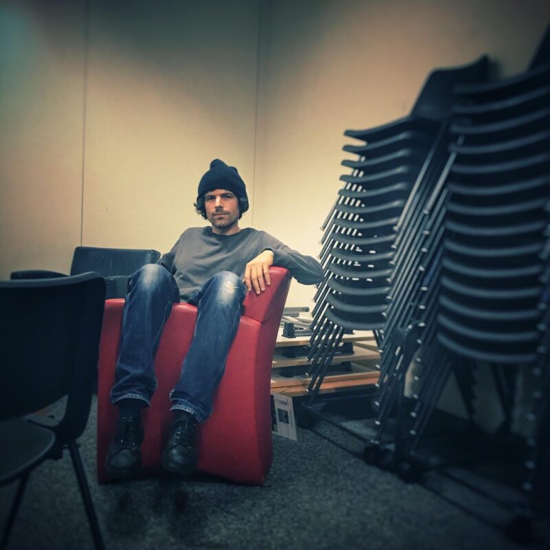 Ein Mann mit Beanie sitzt in einem roten Sessel.