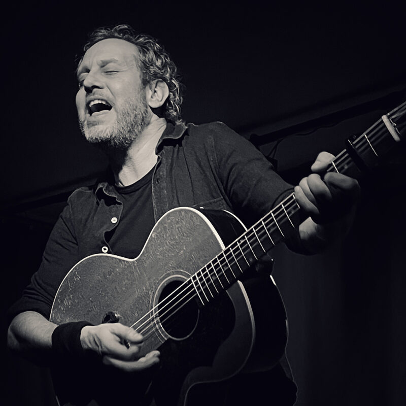 Mann singt leidenschaftlich und spielt akustische Gitarre in Schwarz-Weiß.