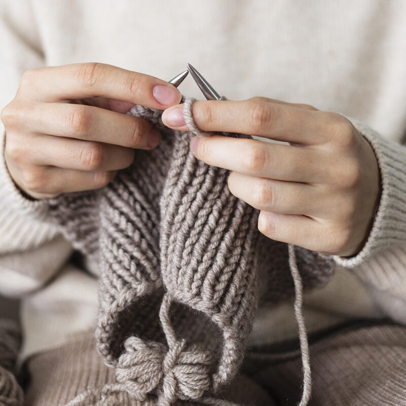 Hände, die mit brauner Wolle und Stricknadeln stricken.
