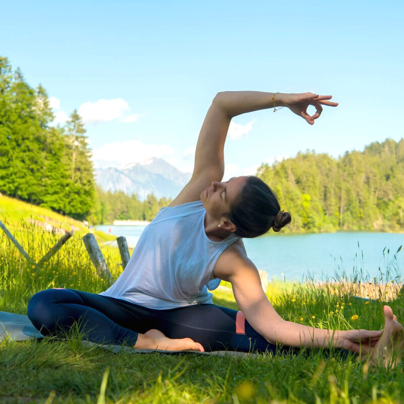 Frau praktiziert Yoga im Freien vor einem Bergsee.